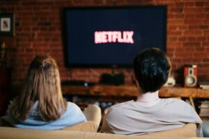 couple sits on the couch watching the netflix logo power up on the tv